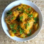 Instant Pot Indian Chicken Curry in a white bowl on a straw background; garnished with chopped cilantro