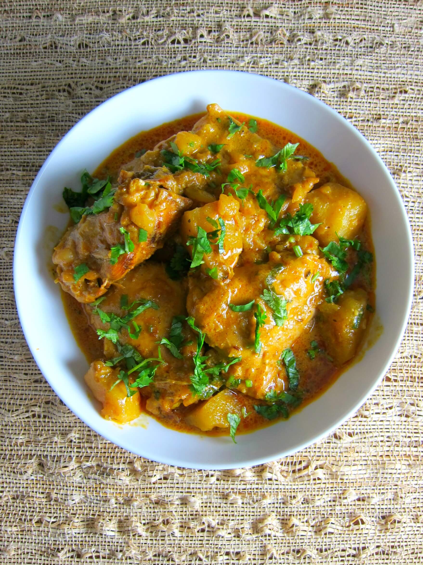 Instant Pot Indian Chicken Curry in a white bowl on a straw background; garnished with chopped cilantro