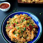 Instant Pot Jambalaya in blue bowl with hot sauce, stack of plates in background on a black table - Paint the Kitchen Red