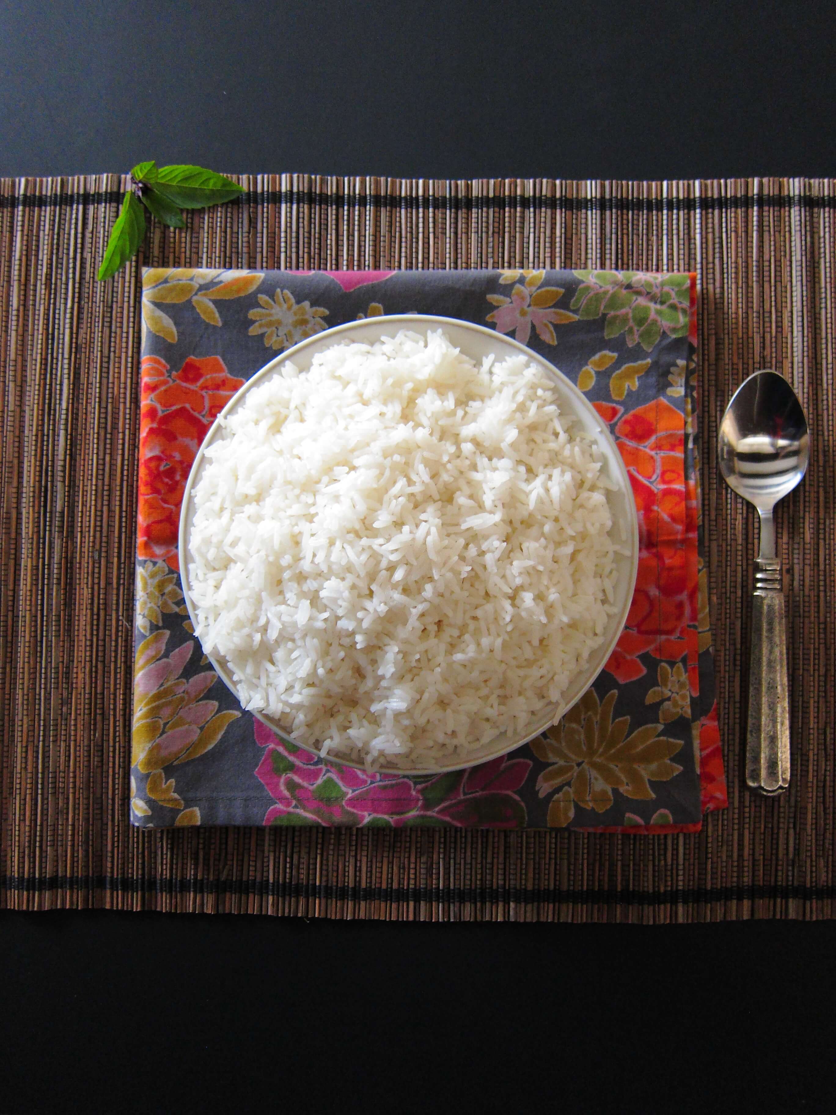 Instant Pot Jasmine Rice in white bowl on flowery colorful napkin and straw placemat with a spoon- Paint the Kitchen Red