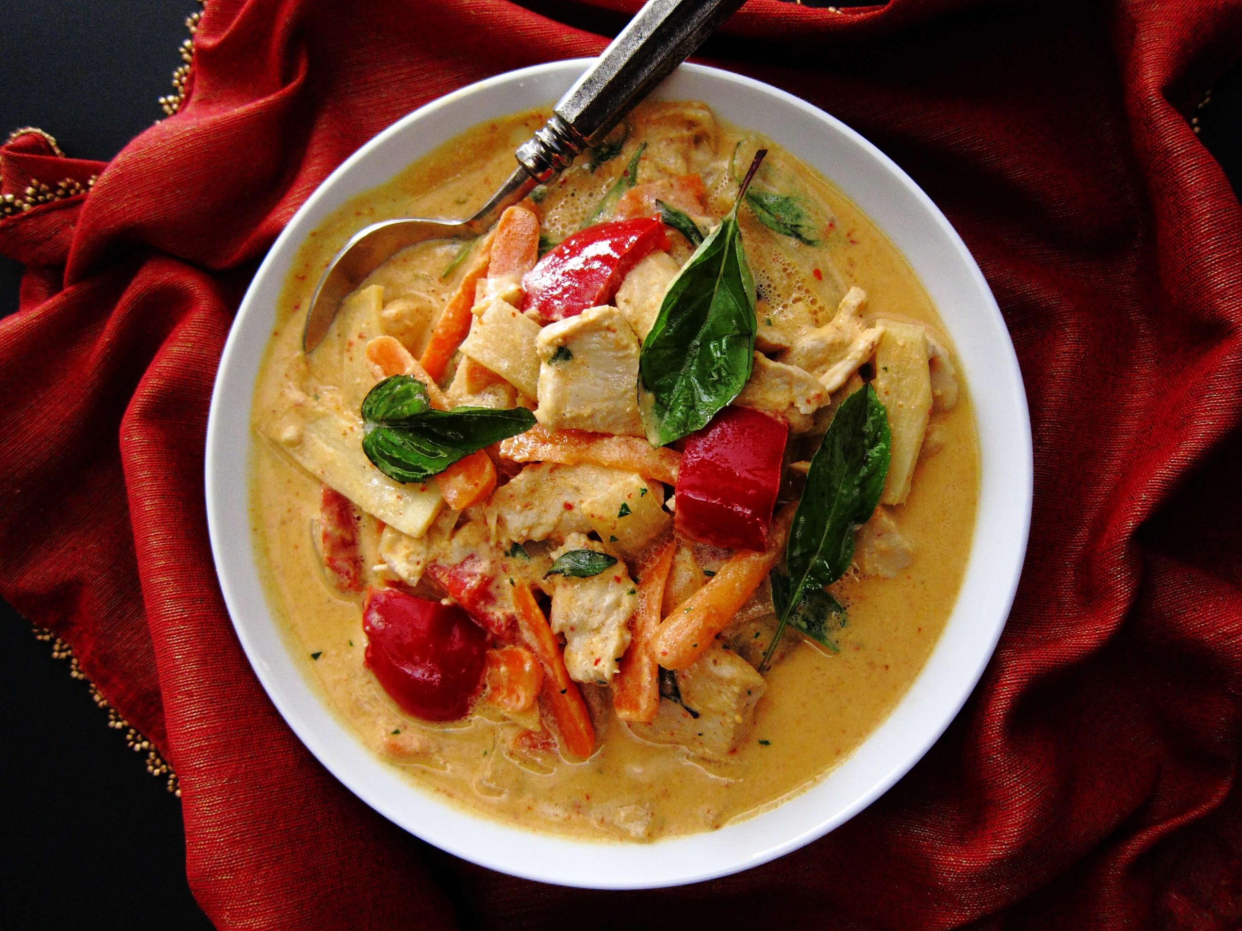 Instant Pot Thai Red Curry with colorful vegetables in white bowl with spoon on rich red napkin.