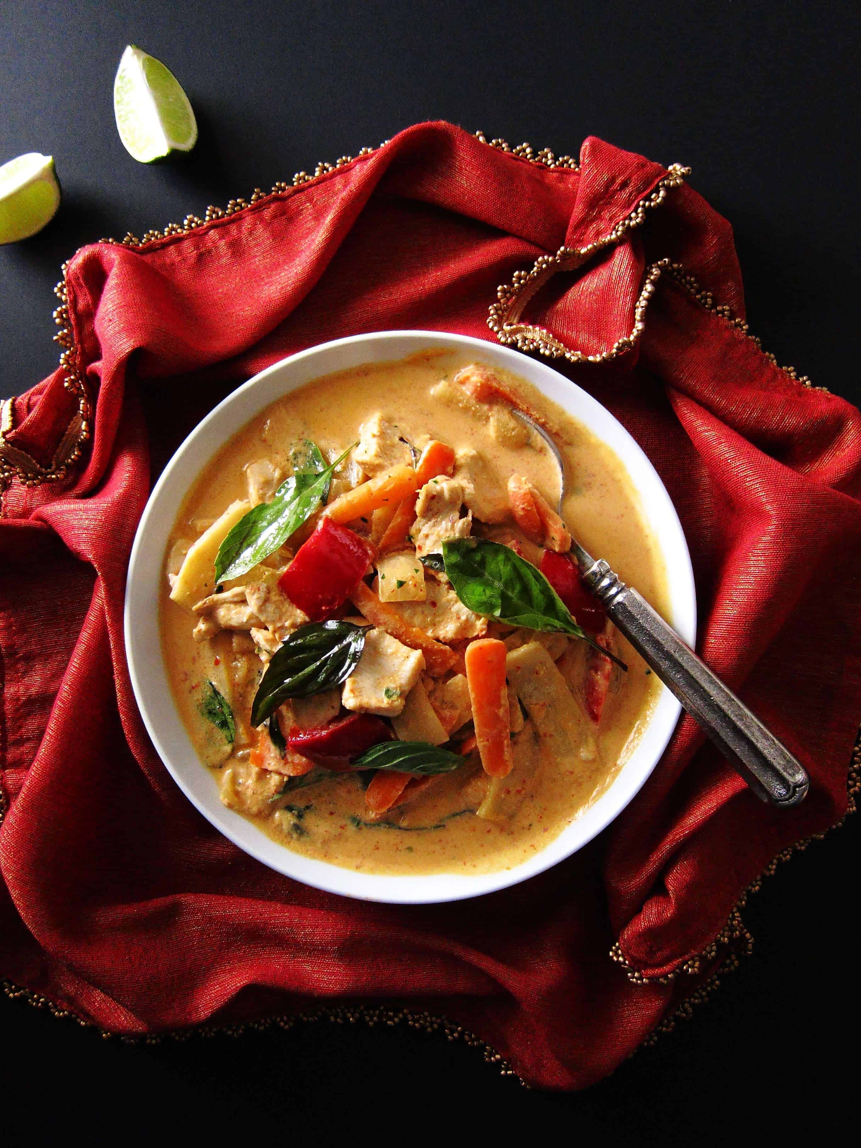 Instant Pot Thai Red Curry Chicken on red napkin with gold and two pieces of lime on black surface - Paint the Kitchen Red