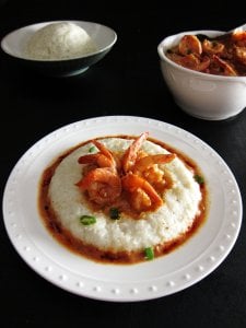 Instant Pot Shrimp and Grits on white plate, black table with rice and shrimp in bowls in the background - Paint the Kitchen Red