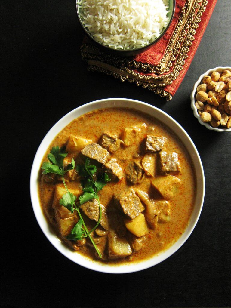 Instant Pot Beef Massaman Curry with beef and potatoes in a white bowl topped with a cilantro sprig