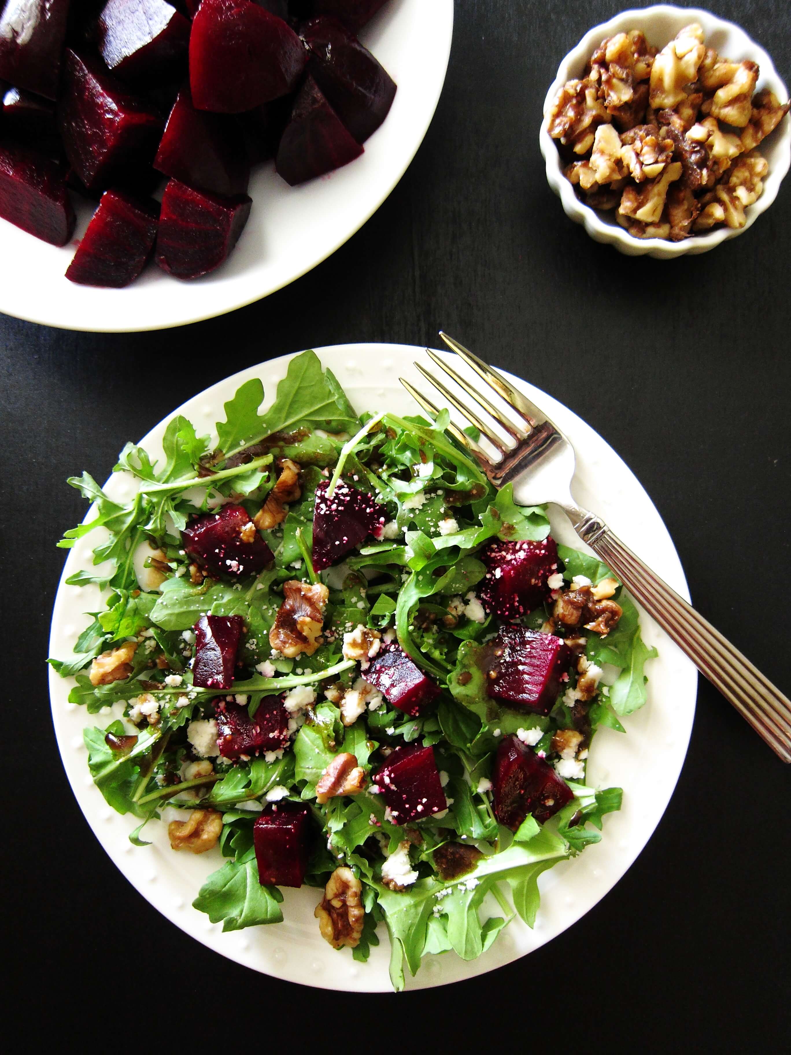 Arugula Goat Cheese Beet Salad on white plate with beets and walnuts on black background