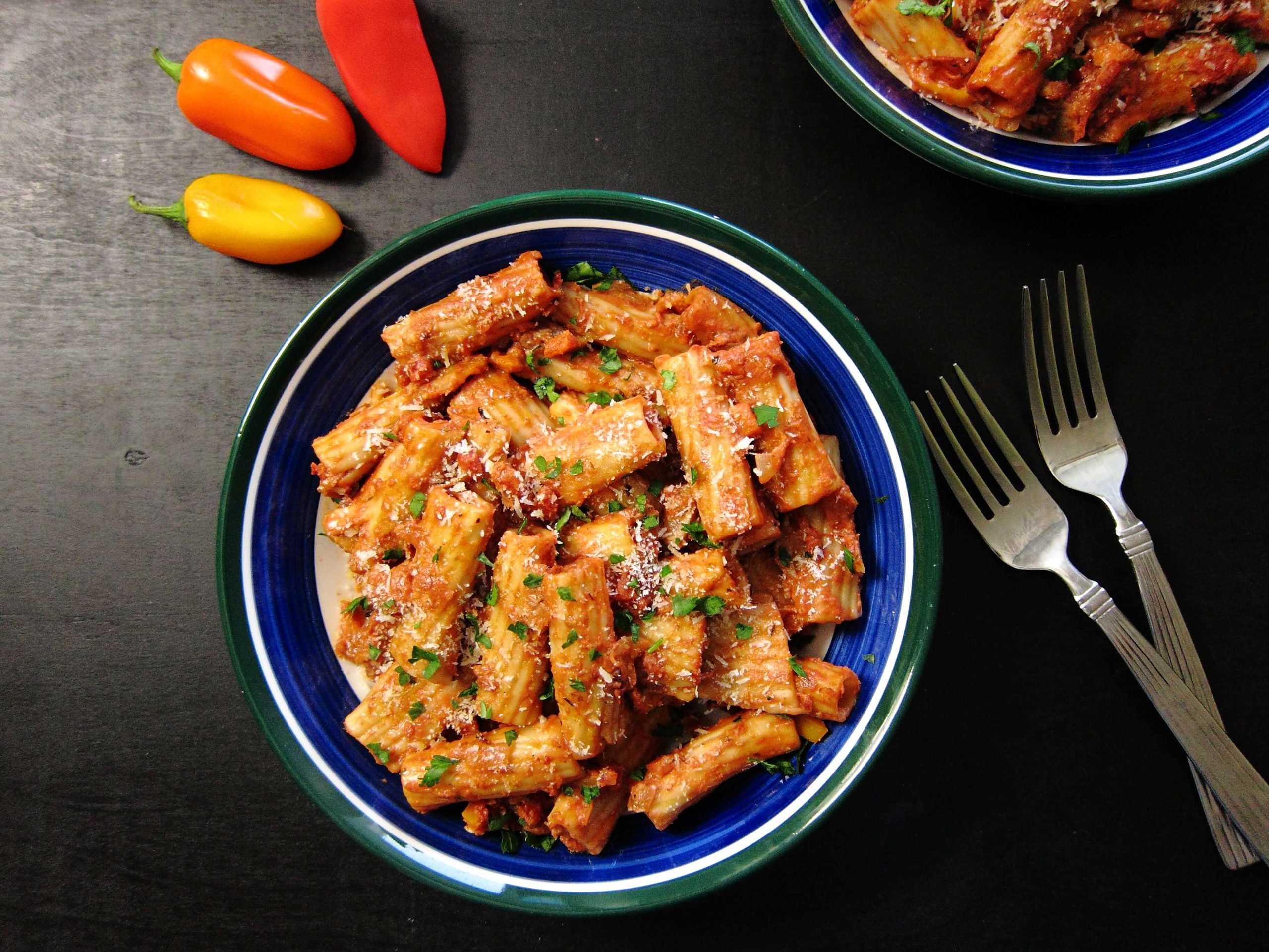 Blue bowl with pasta, sauce and shredded cheese and parsley.