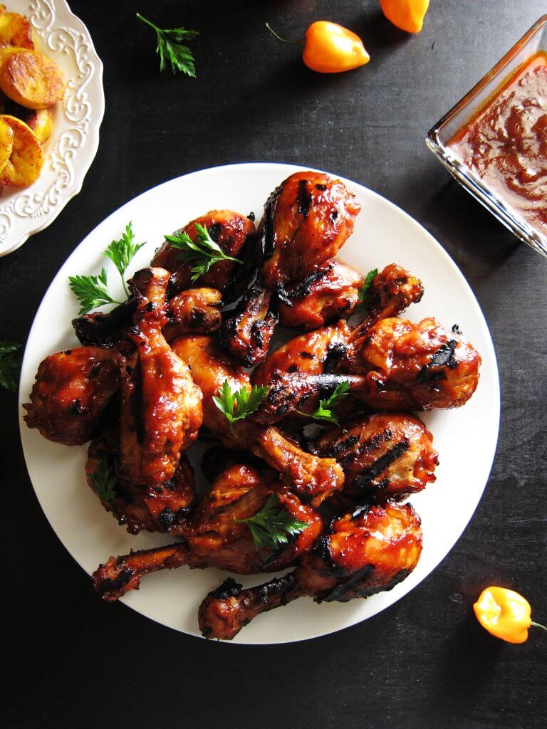 Instant Pot Jamaican Jerk Chicken drumsticks on white plate with hot peppers and fried bananas in background - Paint the Kitchen Red