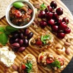 Instant Pot Ratatouille in a bowl and on crusty bread, all on a round wooden board with cherries, cheese, nuts