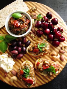 Instant Pot Ratatouille in a bowl and on crusty bread, all on a round wooden board with cherries, cheese, nuts