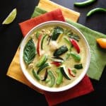 Instant Pot Thai Green Curry with Chicken with colorful green curry in white bowl on three colorful napkins. With lime slice and chilies on a black background- Paint the Kitchen Red