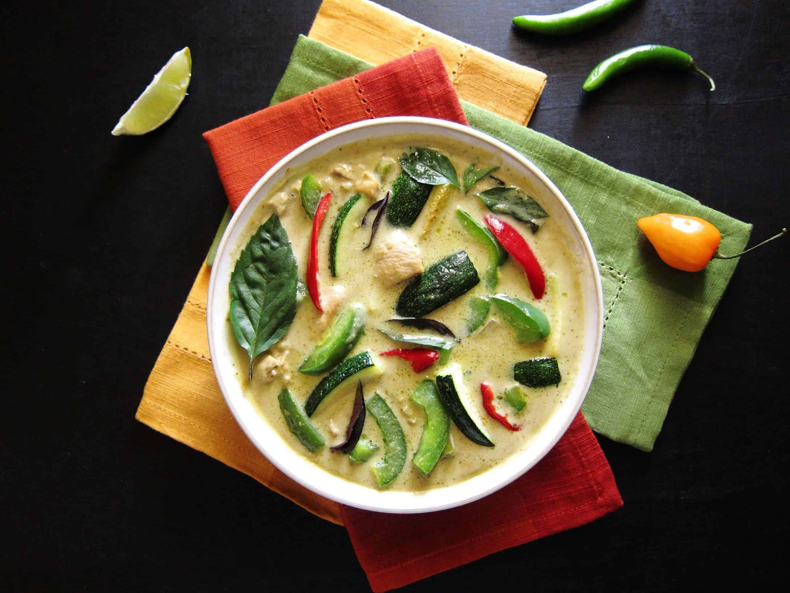 Instant Pot Thai Green Curry with Chicken with colorful green curry in white bowl on three colorful napkins. With lime slice and chilies on a black background- Paint the Kitchen Red