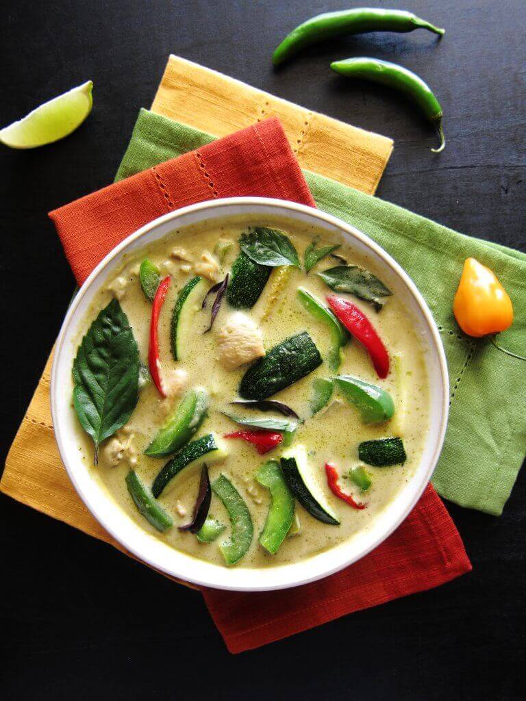 Instant Pot Thai Green Curry with Chicken with colorful green curry in white bowl on three colorful napkins. With lime slice and chilies on a black background- Paint the Kitchen Red