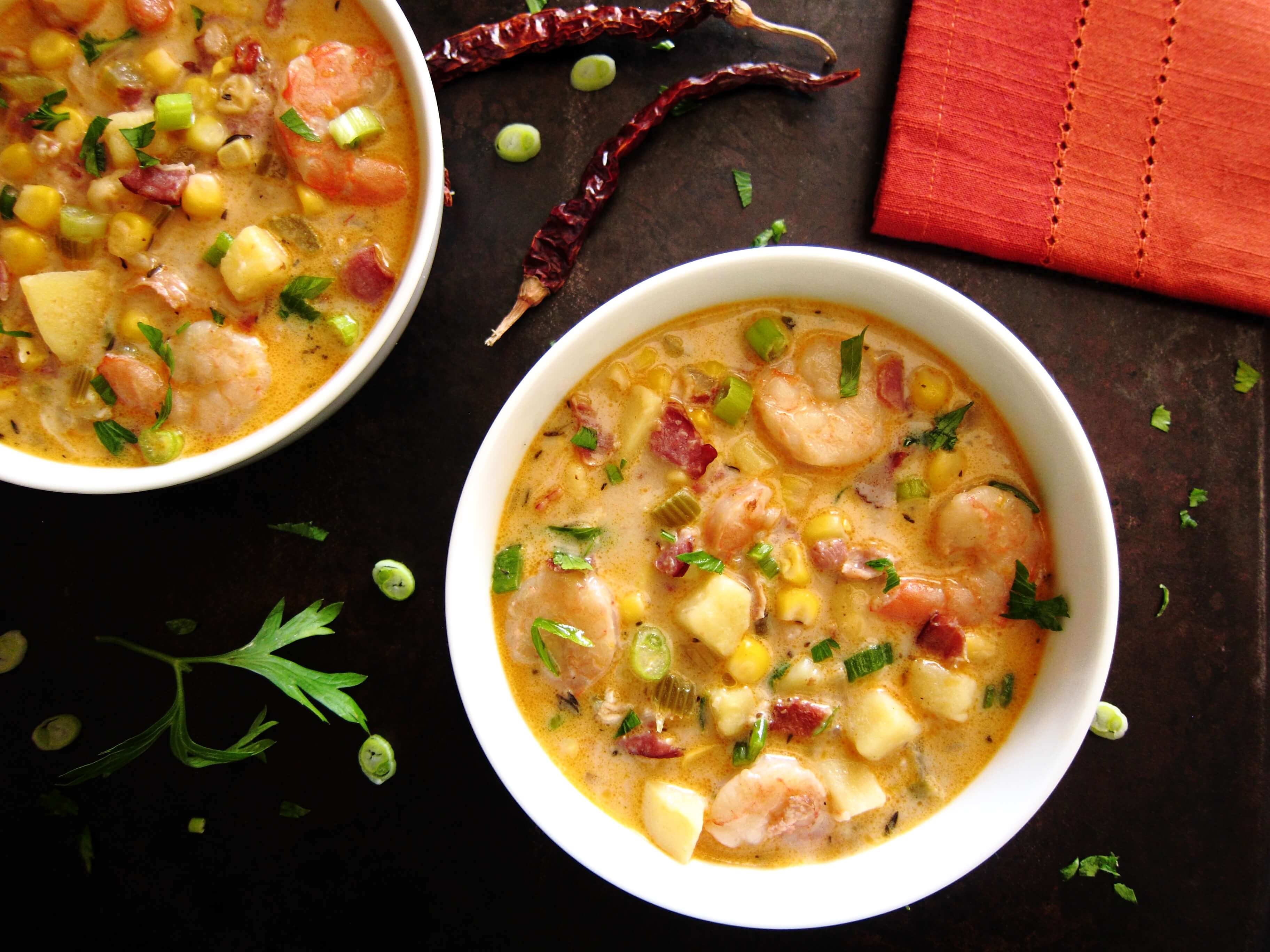 Creamy Instant Pot Chipotle Shrimp Soup colorful with red napkin, dried red chili peppers, parsley and green onions sprinkled on black background - Paint the Kitchen Red