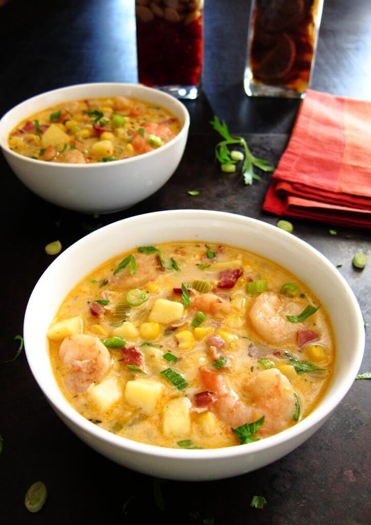 Two white bowls of colorful Creamy Instant Pot Chipotle Shrimp Soup with potatoes, corn, bacon and green onions on black background - Paint the Kitchen Red