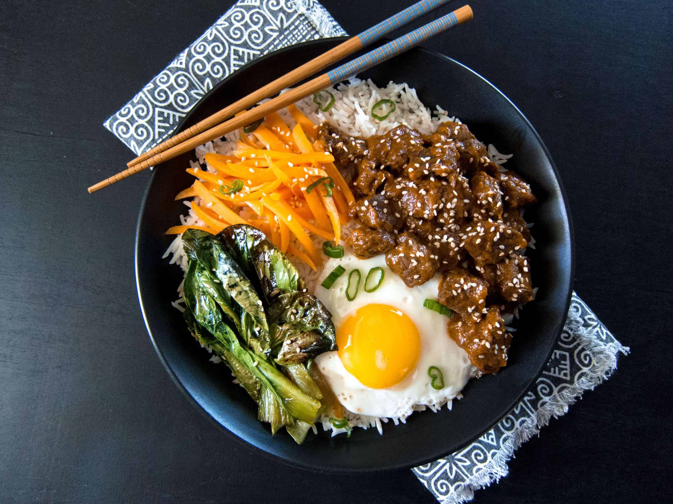 Instant Pot Korean Beef on a bed of rice with sauteed vegetables and fried egg in a black bowl