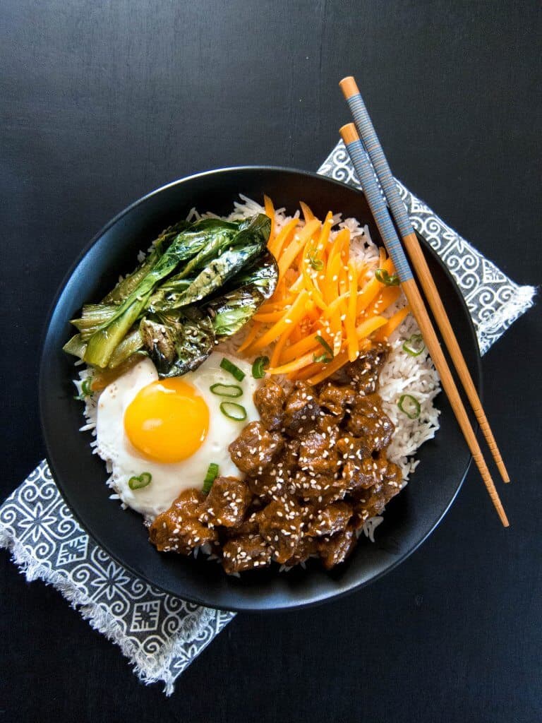 Instant Pot Korean Beef on a bed of rice with sauteed vegetables and fried egg in a black bowl