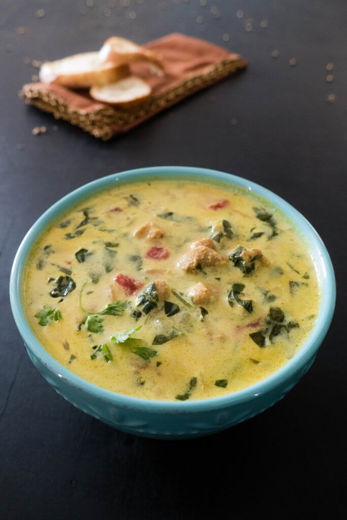 Instant Pot Chicken Curry Soup - yellow colored soup topped with cilantro in teal bowl on black background with brown and gold napkin in distance with french bread slices on top - Paint the Kitchen Red