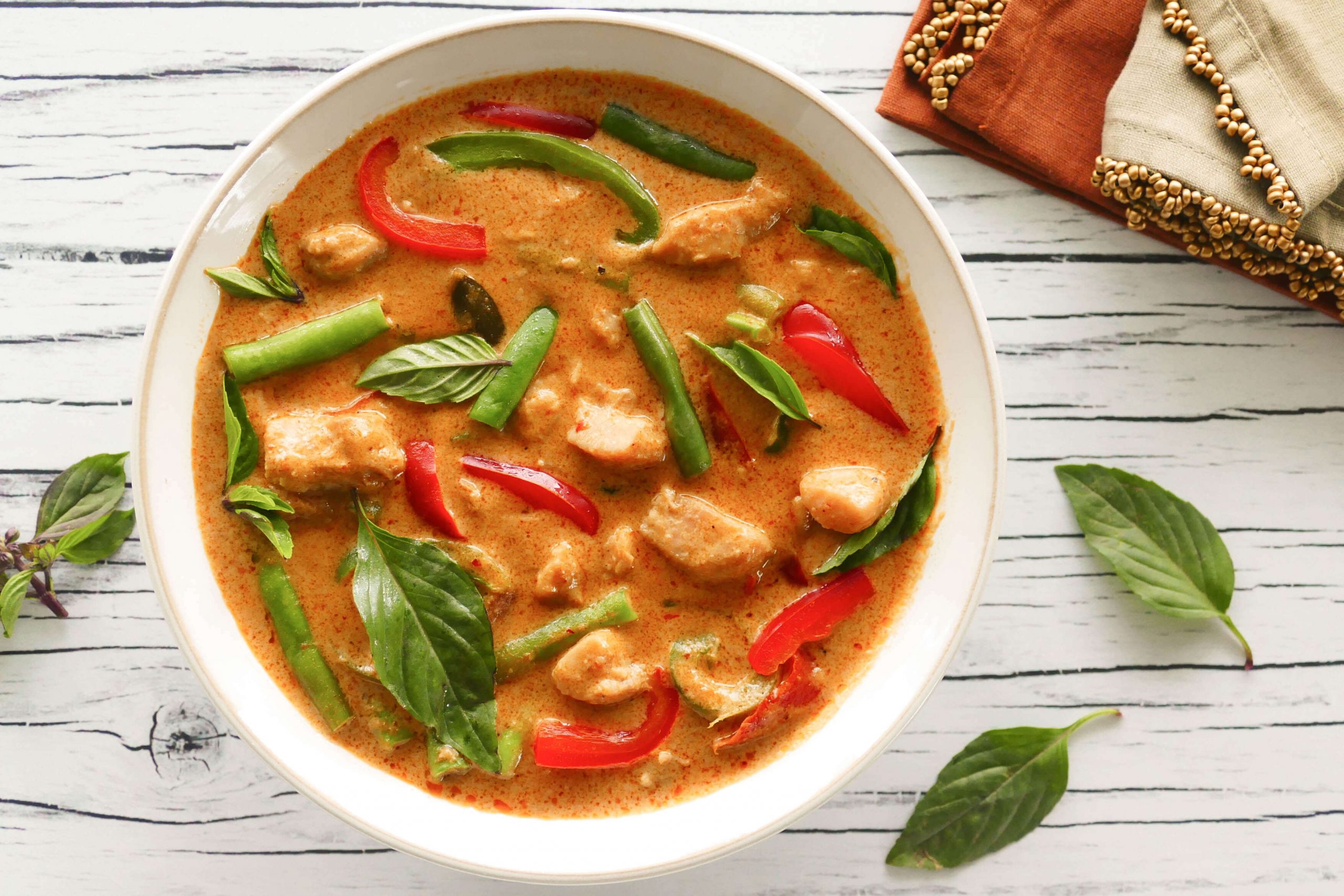 Instant Pot Panang Curry with chicken, green beans, red and green peppers, Thai basil in a white bowl on a light wood background