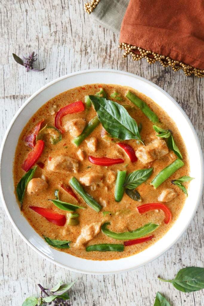 Instant Pot Panang Curry with chicken, green beans, red and green peppers, Thai basil in a white bowl on a light wood background