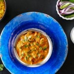 Instant Pot Chicken Tikka Masala in bowl on bright blue plate, with yellow rice, red onions and green chilis and yogurt (raita) in bowls in background - Paint the Kitchen Red