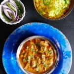 Instant Pot Chicken Tikka Masala in bowl on bright blue plate, with yellow rice, red onions and green chilis and yogurt (raita) in bowls in background - Paint the Kitchen Red