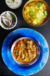 Instant Pot Chicken Tikka Masala in bowl on bright blue plate, with yellow rice, red onions and green chilis and yogurt (raita) in bowls in background - Paint the Kitchen Red