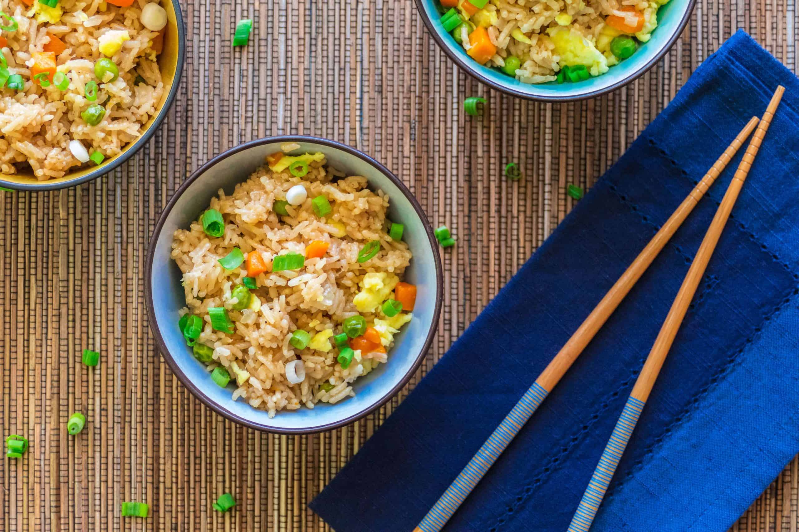 Instant Pot Fried Rice - bowl of rice with vegetables garnished with green onions in blue bowl on blue napkin with chopsticks