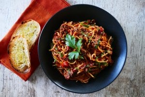 Instant Pot Spaghetti and Meat Sauce in a black bowl and wood background; napkin with bread on the side - Paint the Kitchen Red