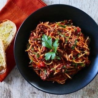 Instant Pot Spaghetti and Meat Sauce in a black bowl and wood background; napkin with bread on the side - Paint the Kitchen Red