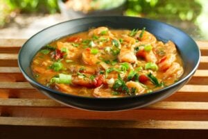 Instant Pot Shrimp Etouffee garnished with green onions and chopped parsley in black bowl on a wood slat background - Paint the Kitchen Red