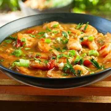 Instant Pot Shrimp Etouffee garnished with green onions and chopped parsley in black bowl on a wood slat background - Paint the Kitchen Red