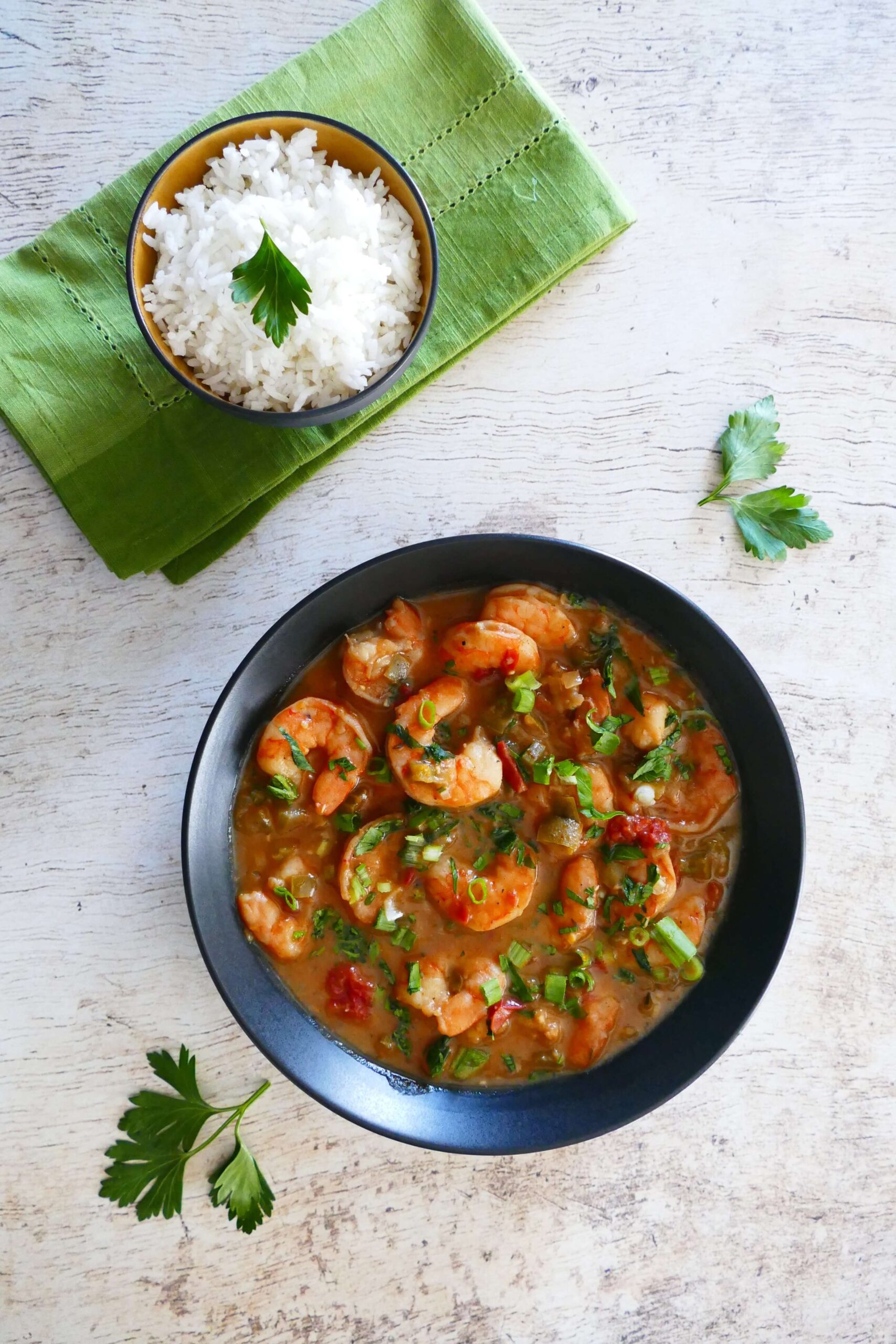 Instant Pot Shrimp Etouffee garnished with green onions and chopped parsley in black bowl with rice in a bowl on a green napkin - Paint the Kitchen Red
