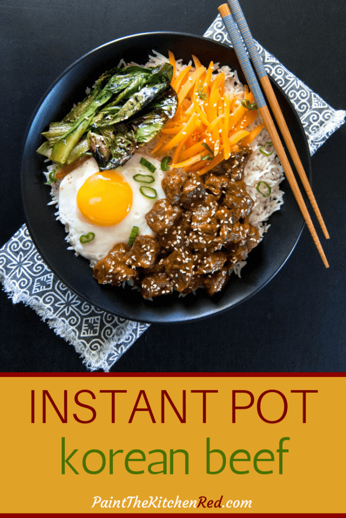 A rice bowl with beef, fried egg, carrots, greens in black bowl with chopsticks and text "instant pot korean beef Paint the Kitchen Red"