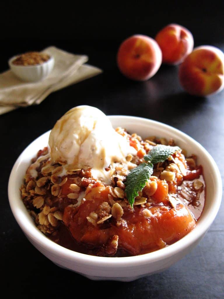 Instant Pot Peach Crisp in white bowl with vanilla ice cream on top - Paint the Kitchen Red