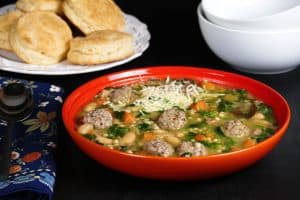 Instant Pot Italian Wedding Soup - Orange bowl with beans, carrots, meatballs, spinach, parmesan and bread and empty bowls in the background - Paint the Kitchen Red