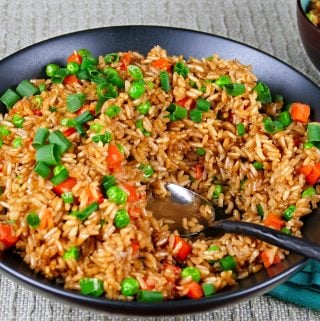 Instant Pot Brown Fried Rice L1 - black bowl of fried rice with carrots peas and green onions with a serving spoon in the middle of bowl - Paint the Kitchen Red