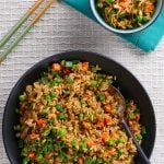 Instant Pot Brown Fried Rice P1 - black bowl of fried rice with carrots peas and green onions with a serving spoon in the middle of bowl