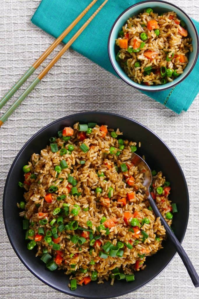 Instant Pot Brown Fried Rice P1 - black bowl of fried rice with carrots peas and green onions with a serving spoon in the middle of bowl 