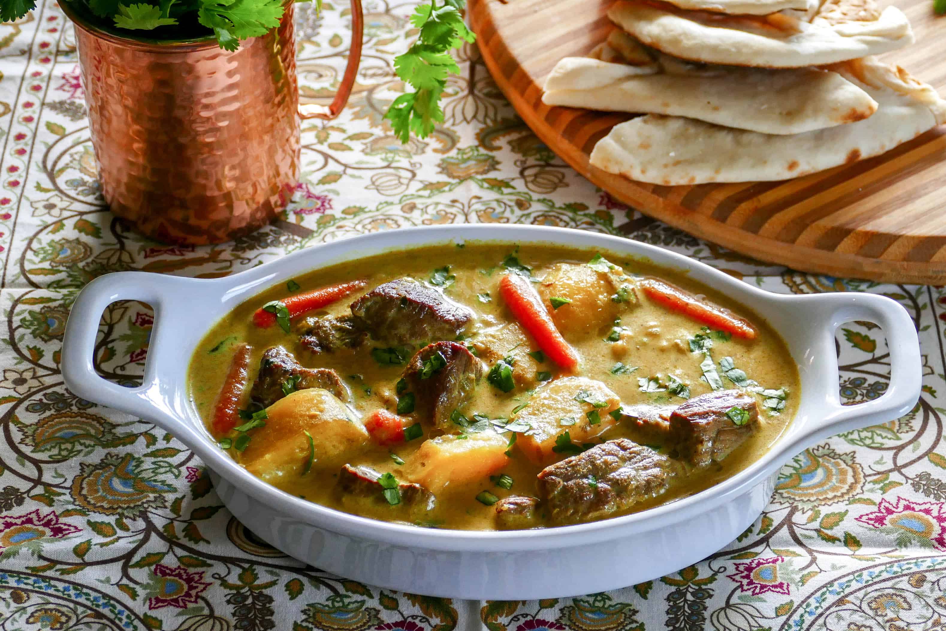 Instant Pot Beef Curry in white oval serving dish with cilantro and naan in the background - Paint the Kitchen Red.jpg