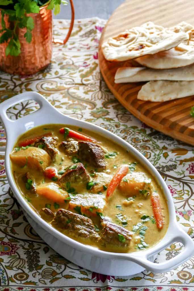 Instant Pot Beef Curry in white oval serving dish with cilantro and naan in the background - Paint the Kitchen Red.jpg