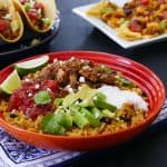 Instant Pot Chicken Tinga rice bowl in orange bowl with chicken tinga tacos and nachos in the background - Paint the Kitchen Red