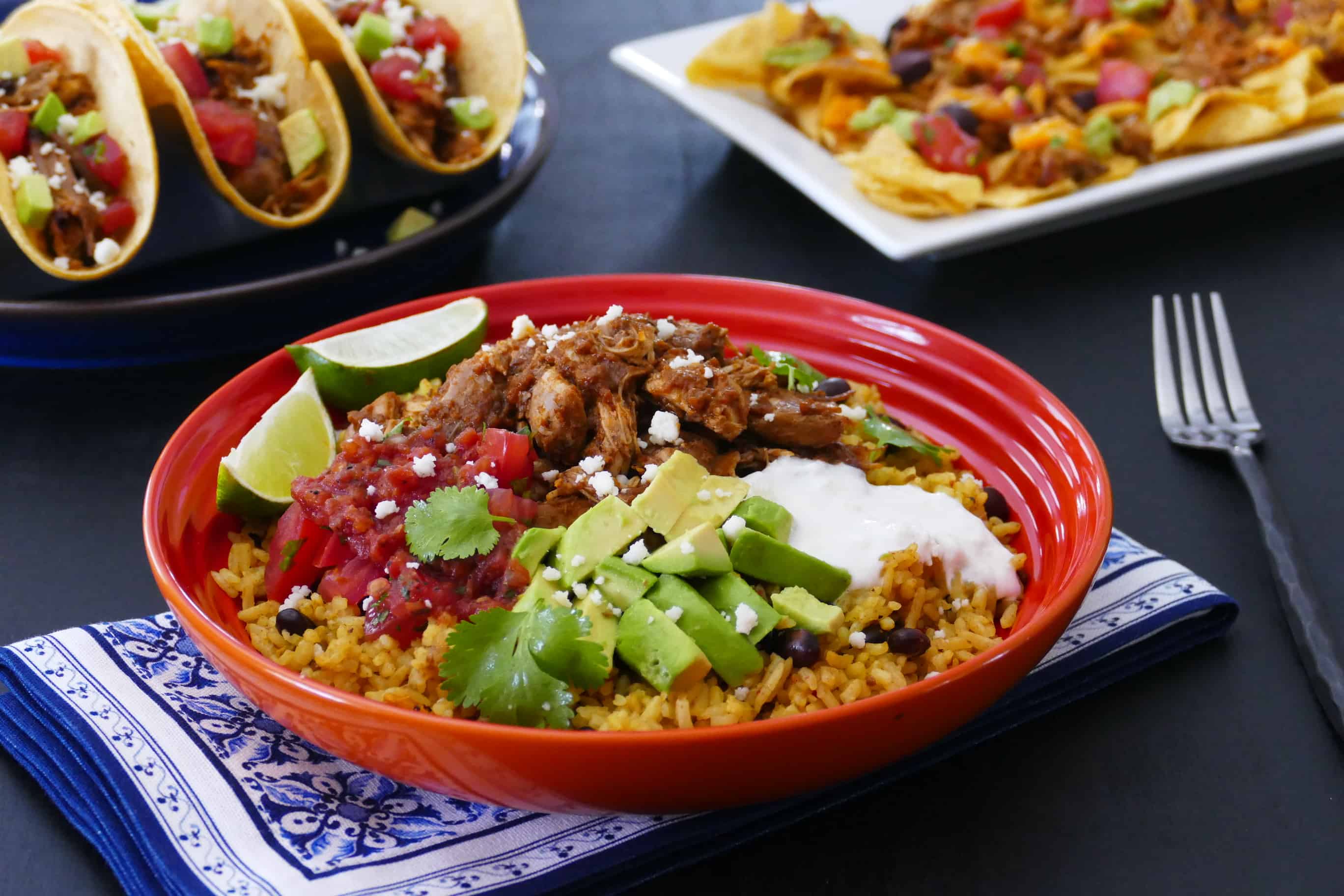 Instant Pot Chicken Tinga rice bowl in orange bowl with chicken tinga tacos and nachos in the background - Paint the Kitchen Red