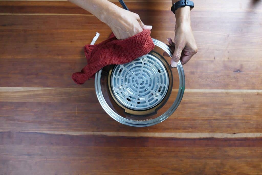 Damp red cloth being used to wipe the upside down Mealthy CrispLid - Paint the Kitchen Red