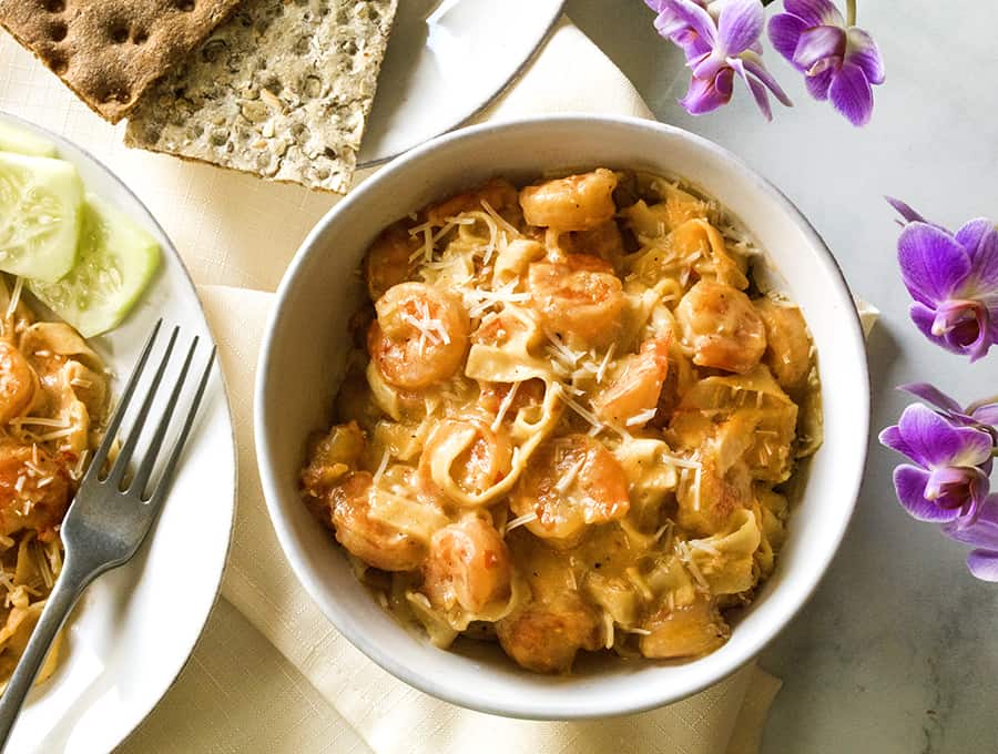 Shrimp scampi in a bowl with a plate of crackers on the side and pink flowers in background