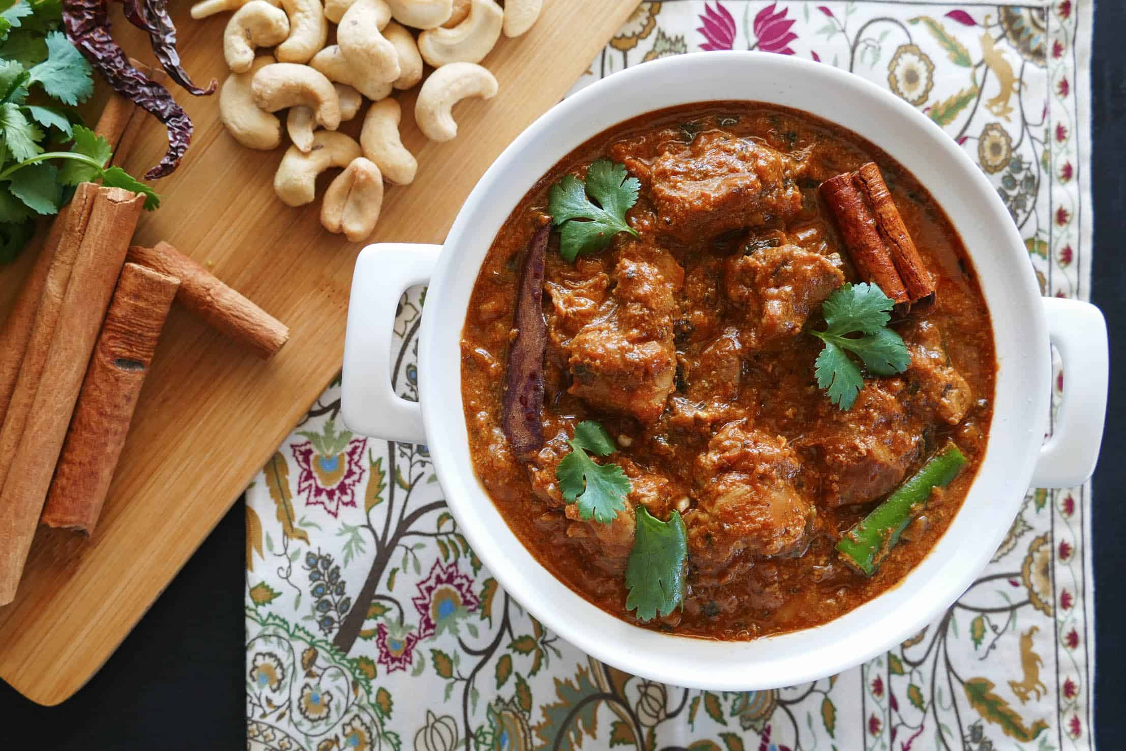 Instant Pot Cashew Butter Chicken in white bowl on flowered napkin, with cinnamon, cilantro, cashews in background - Paint the Kitchen Red