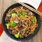 Instant Pot Lo Mein with Beef and Broccoli in black bowl on straw mat with chopsticks laid across bowl - Paint the Kitchen Red