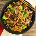 Instant Pot Lo Mein with Beef and Broccoli in black bowl on straw mat with chopsticks laid across bowl - Paint the Kitchen Red