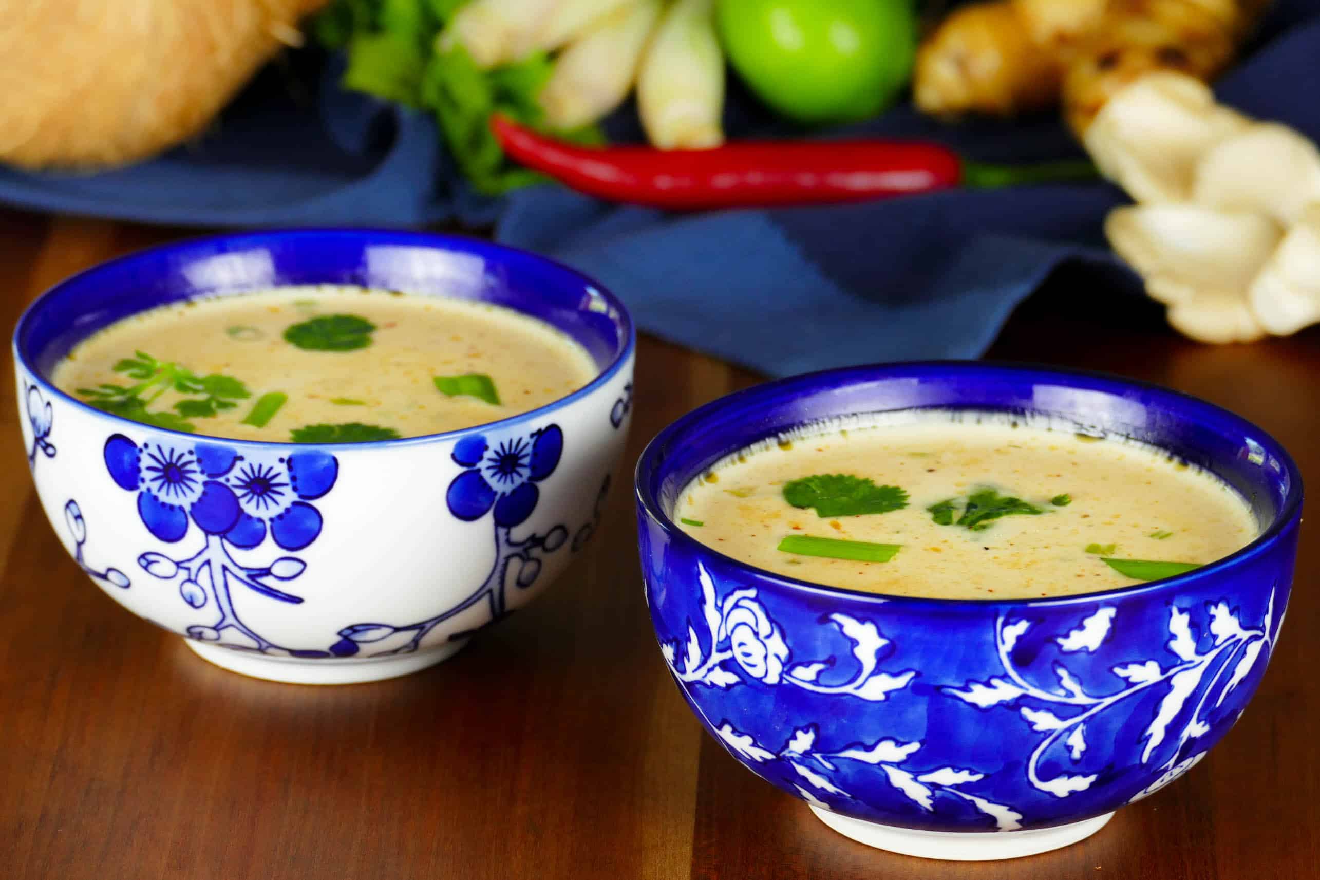 2 Asian-print bowls of Instant Pot Thai coconut soup with herbs in the background
