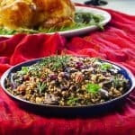 Instant Pot Wild Rice Pilaf topped with pecans and dried cranberries in a blue bowl on a festive red tablecloth- Paint the Kitchen Red