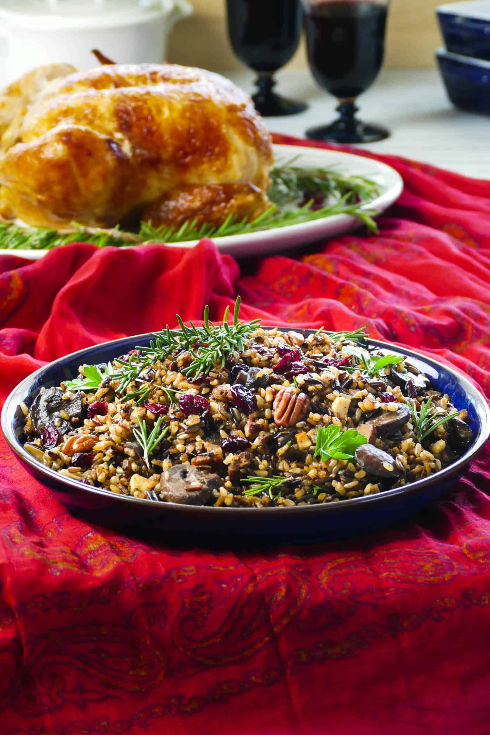 Instant Pot Wild Rice Pilaf topped with pecans and dried cranberries in a blue bowl on a festive red tablecloth- Paint the Kitchen Red